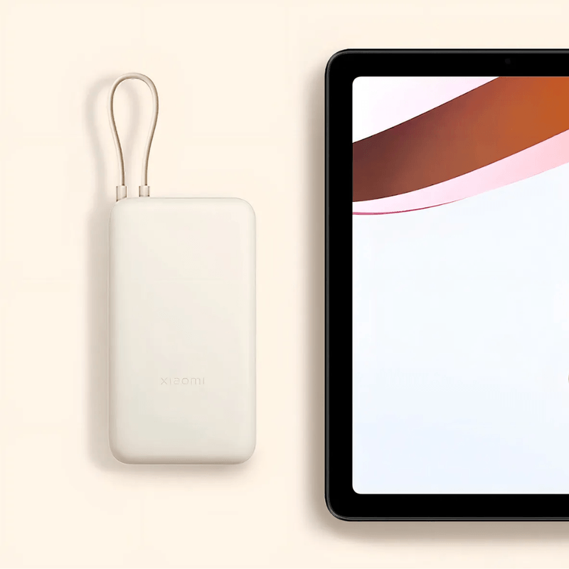 Power Bank Xiaomi 20000mAh 33W, carga rápida, hasta múltiples cargas, beige, ángulo frontal junto a una tablet